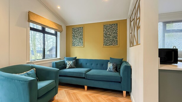 Una sala de estar con un sofá, un sillón, una ventana y una obra de arte colgada en la pared.