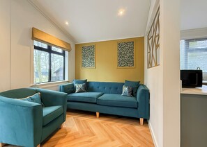 Una sala de estar con un sofá, un sillón, una ventana y una obra de arte colgada en la pared.