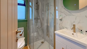 A modern bathroom with a glass shower enclosure, a white sink with gold fixtures, and a green accent wall. - 1 bedroom accommodation in Millom (Millom)