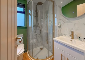 A modern bathroom with a glass shower enclosure, a white sink with gold fixtures, and a green accent wall.