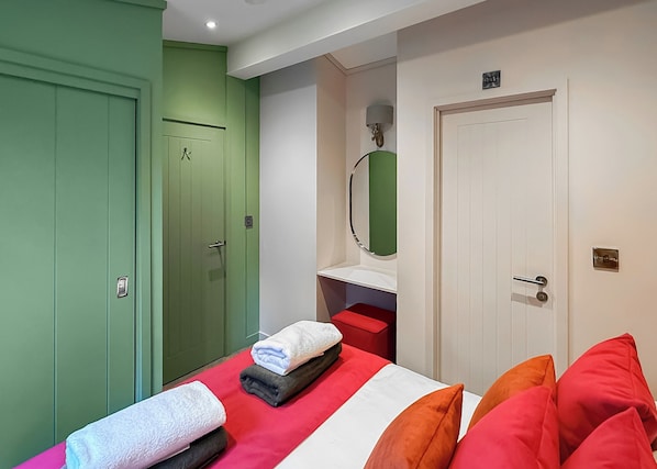 A room with a bed, a green wardrobe, a white door, a mirror, and a red bench.