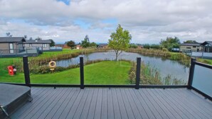 A deck with a view of a pond, surrounded by grass and a few trees. - 1 bedroom accommodation in Llanon (Llanon)