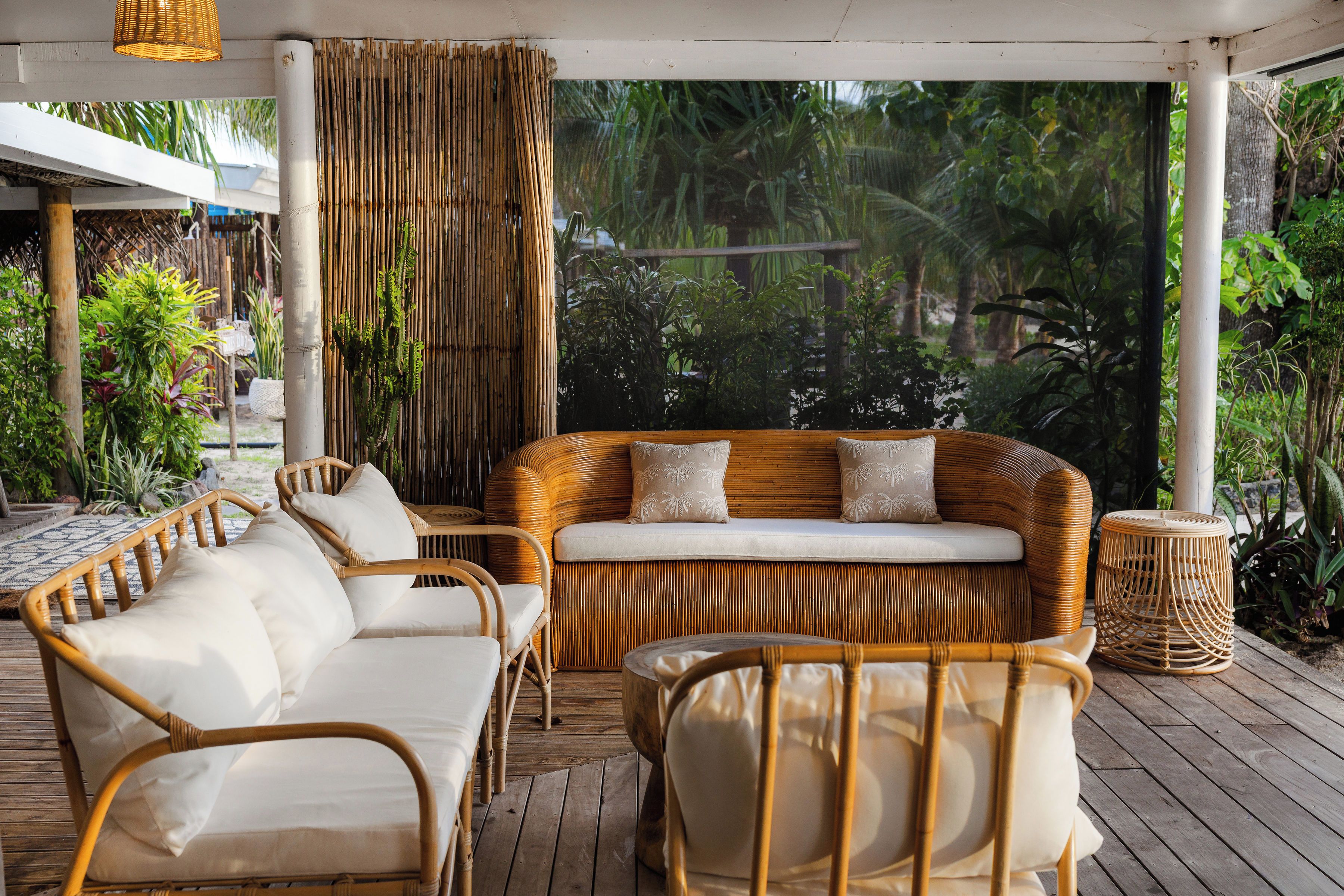 A covered outdoor seating area with wicker furniture and a view of lush greenery.
