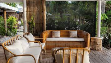 A covered outdoor seating area with wicker furniture and a view of lush greenery.
