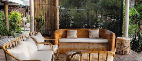 A covered outdoor seating area with wicker furniture and a view of lush greenery.
