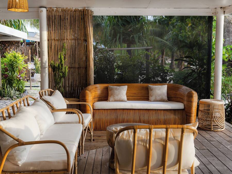 A covered outdoor seating area with wicker furniture and a view of lush greenery.