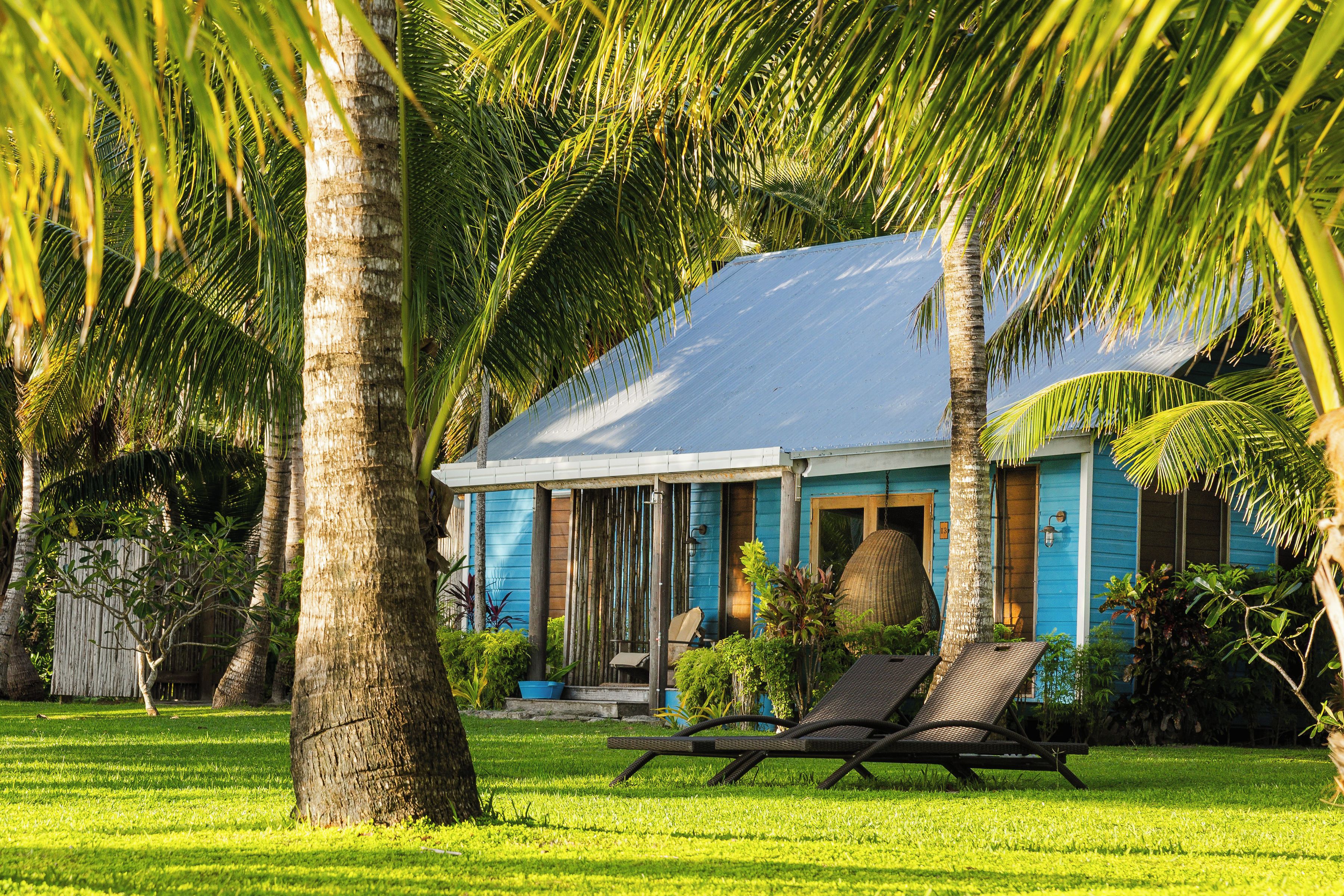 A house with a blue exterior, a covered porch, and a lawn with a lounge chair.