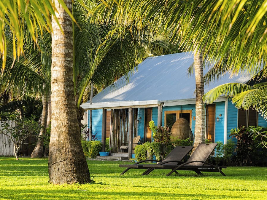 Una casa con fachada azul, un porche cubierto y un césped con una silla de descanso.