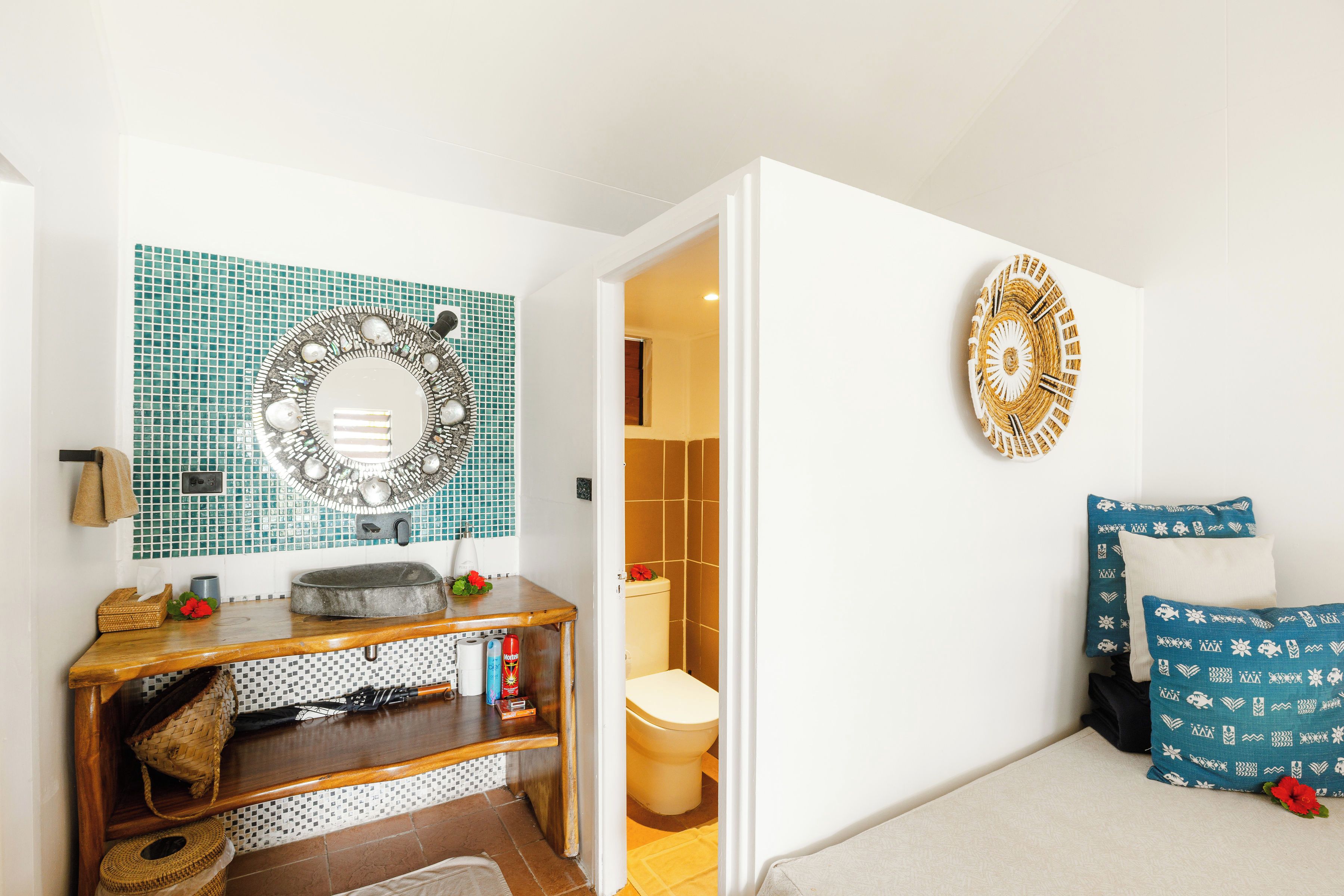 A bathroom with a sink, mirror, and toilet. There is a towel rack and a shelf with toiletries.