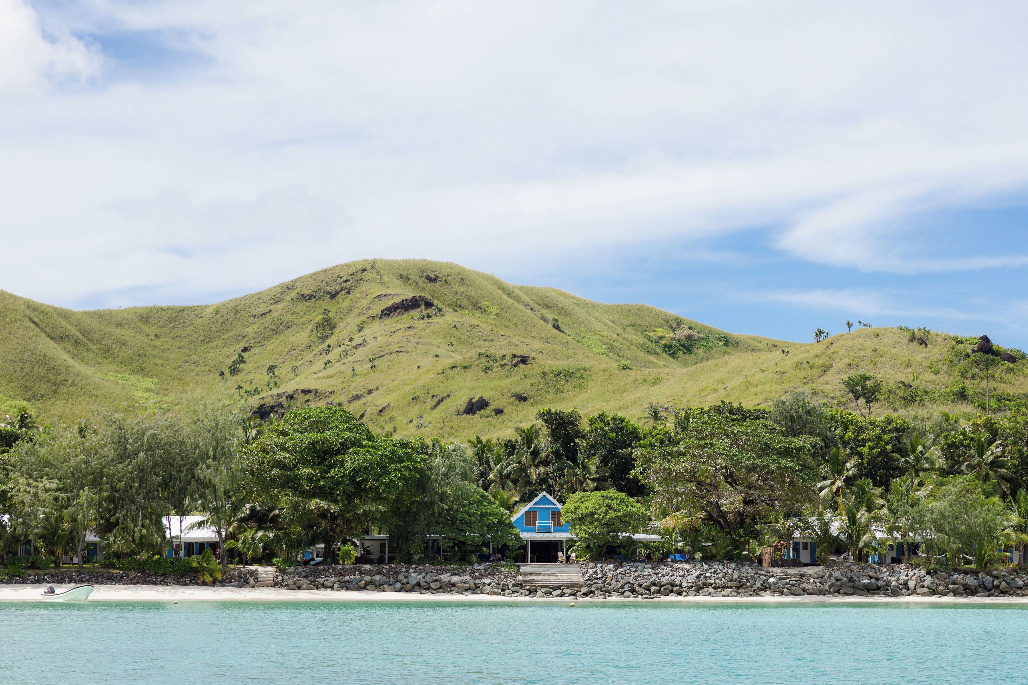 A coastal landscape with a hill, a beach, and a building with a blue roof.