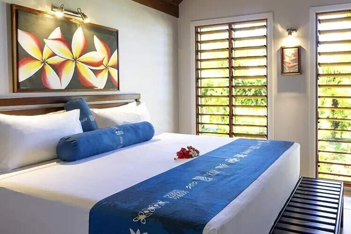 Un cuarto de hotel con una cama, un cuadro, una ventana con persianas y una pequeña foto en la pared.