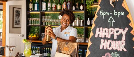A bar area with a bartender, shelves of liquor bottles, glasses, and a chalkboard sign indicating happy hour.