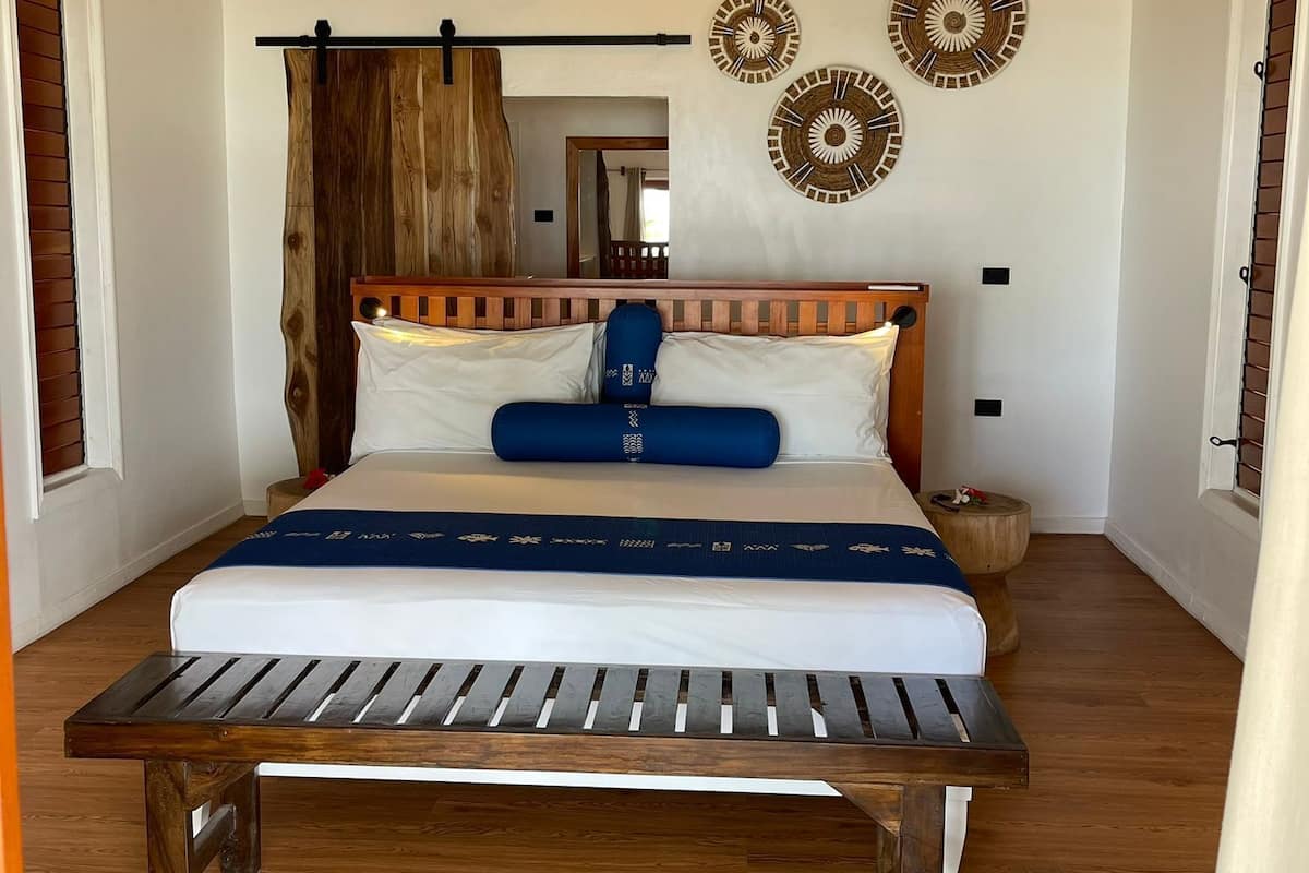 Un dormitorio con una cama de madera, una lámpara colgante y detalles decorativos en la pared.