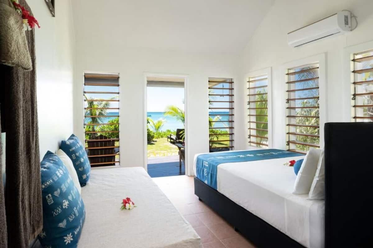 Habitación de hotel con dos camas, vista al océano y balcón.