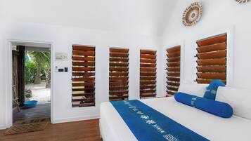 A bedroom with a bed, wooden shutters, a blue bed runner, and a view of the outdoors.