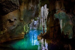 Caverna com estalactites e estalagmites, um lago de água e uma pessoa tirando uma foto.