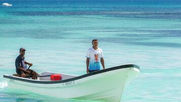 A small boat with two people on it, one seated and one standing, in clear turquoise waters.