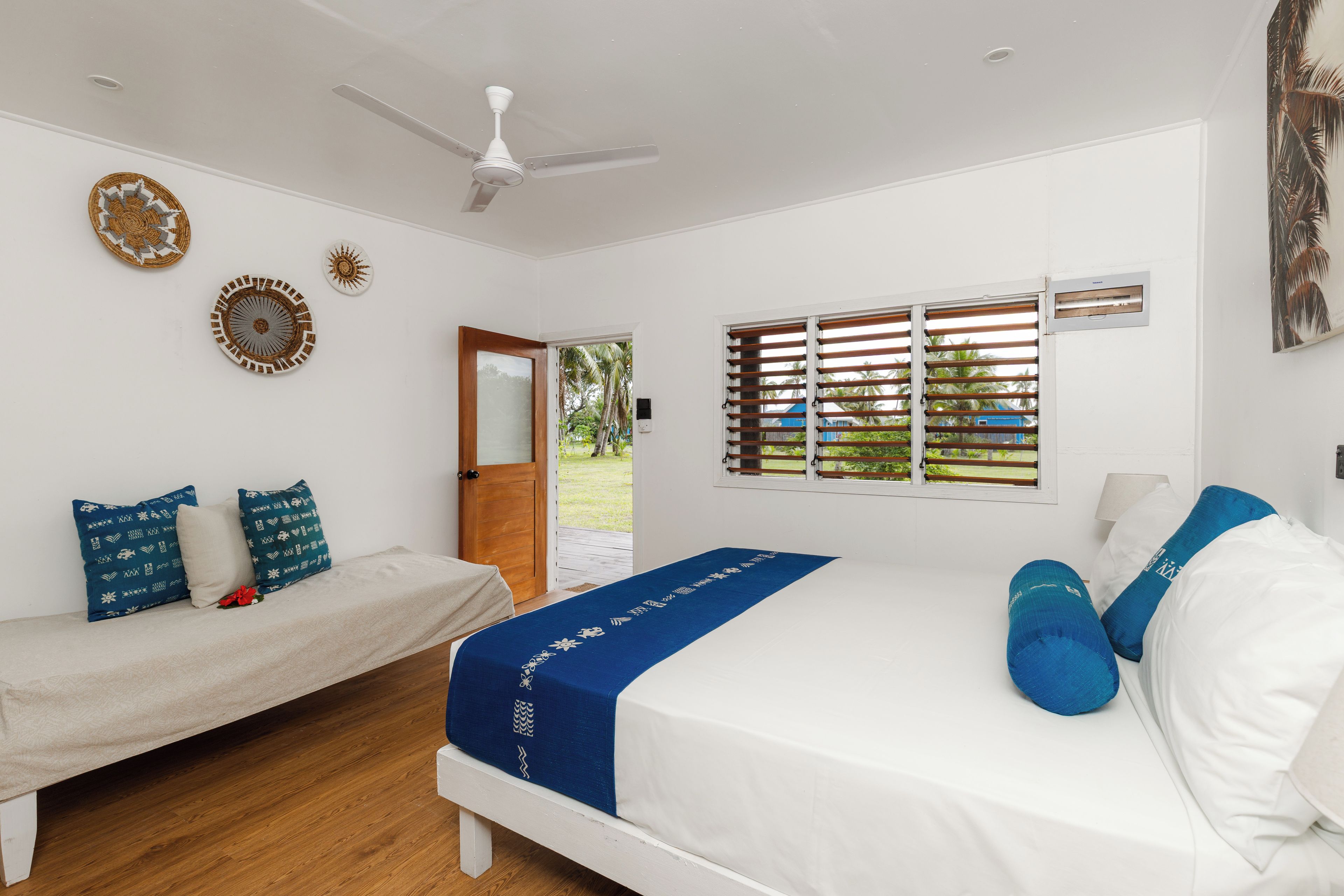 A bedroom with a bed, a bench, a ceiling fan, and a window with blinds.