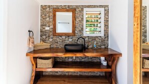 A bathroom with a stone wall, wooden vanity, and a mirror. - Oarsman's Bay Lodge - Adults Only (Nacula Island)
