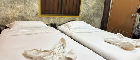 Two single beds with white linens and towels, a window with wooden bars, and a wooden door.