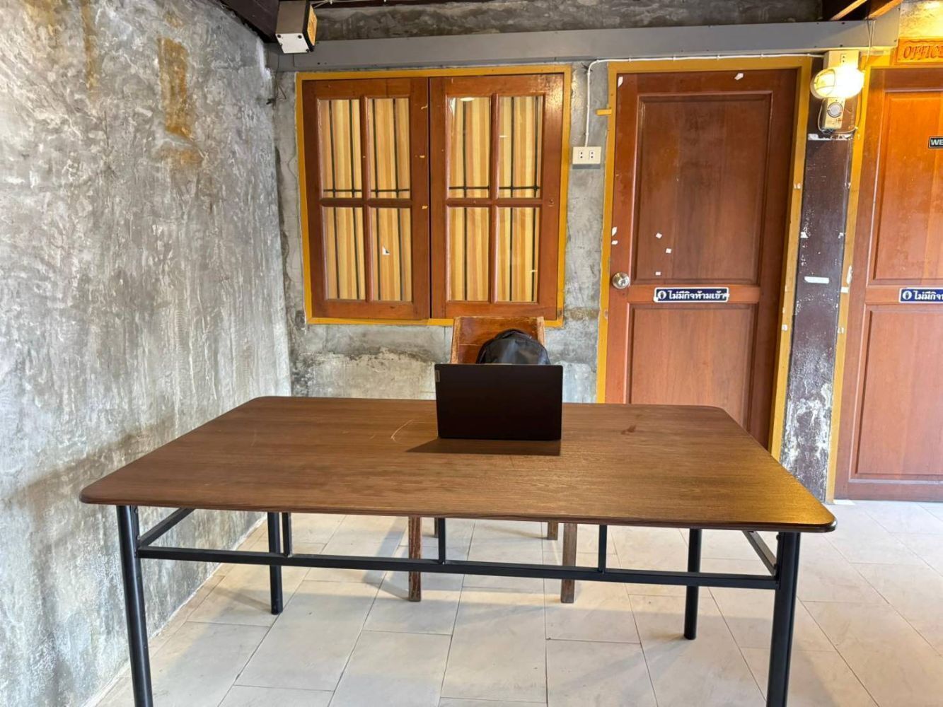 Une table en bois avec un ordinateur portable, un mur en béton et des portes en bois avec une enseigne.
