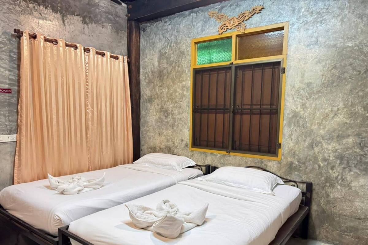 A room with two beds, beige curtains, a window with a decorative frame, and a textured wall.