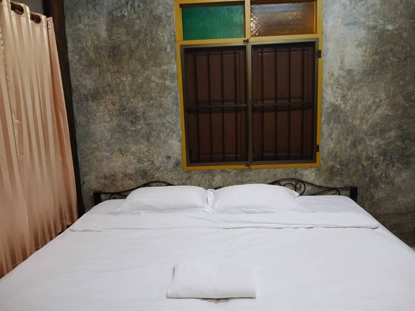 A room with a bed, a window with a wooden shutter, and a curtain.
