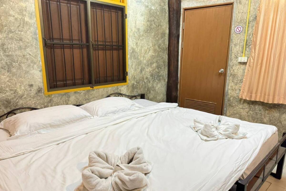 A double bed with white linens and towels, a wooden door, and a window with a metal grill.