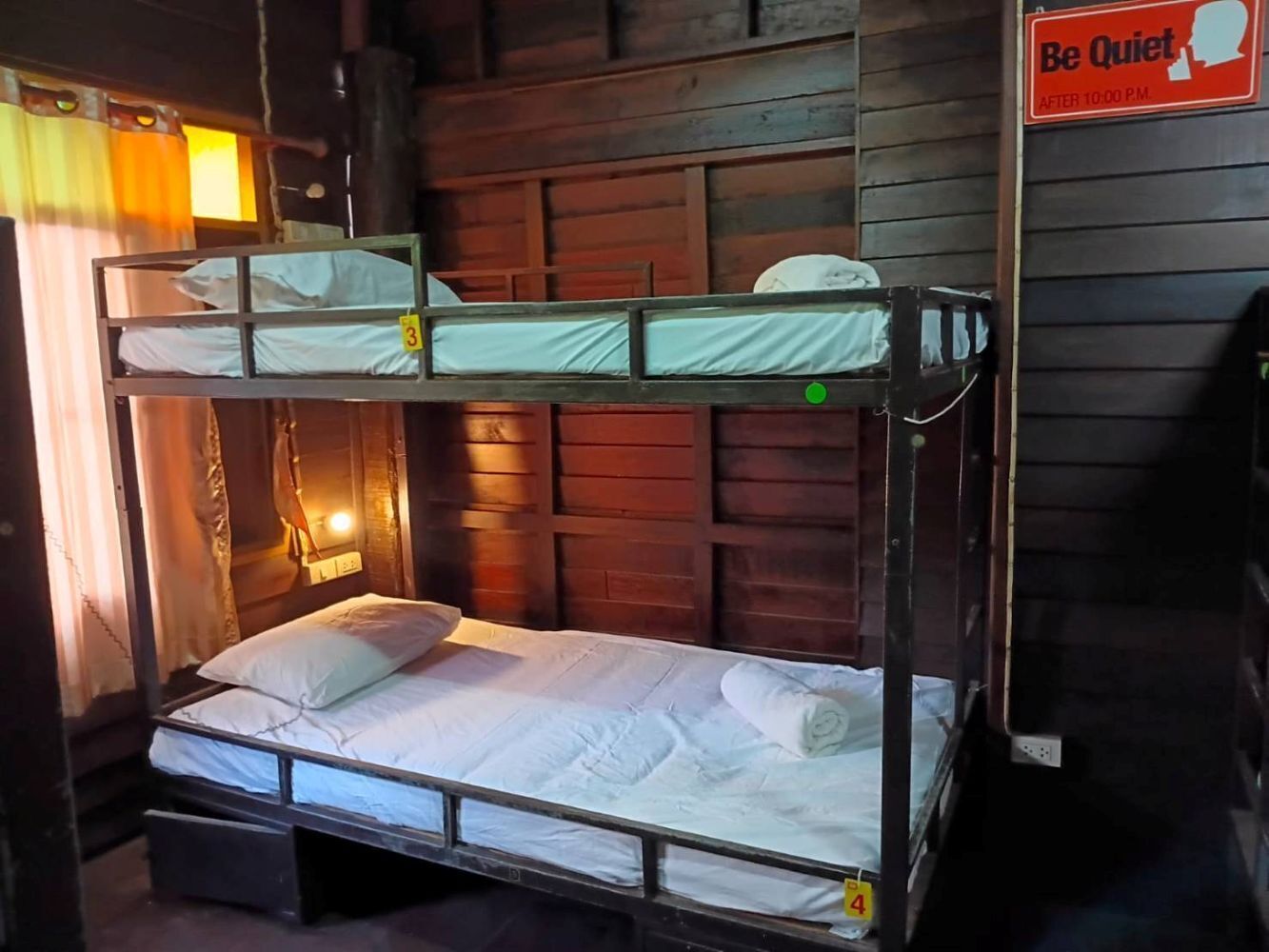 A bunk bed with two levels, a sign indicating quiet hours after 10:00 P.M., and a wall-mounted light fixture.