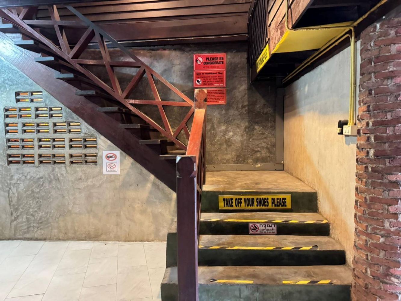 A staircase with a metal handrail, caution signs, and a 'NO DRUGS' sign.
