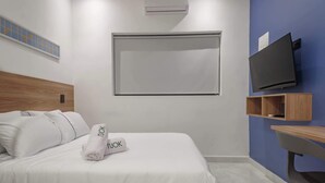 Egy szállodai szoba, amelyben van egy ágy, a falra szerelt televízió és egy fa polc.