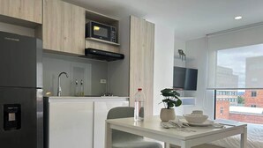 A modern kitchen with a refrigerator, microwave, and sink. There is a dining table with chairs and a potted plant. - NOK Modern Apartment in Chapinero (Bogotá)