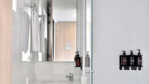 A modern bathroom with a glass shower enclosure, a white sink, and a wooden vanity. - NOK Modern Apartment in Chapinero (Bogotá)
