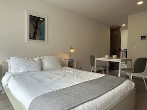 Una habitación de hotel con una cama, un escritorio, una silla, una lámpara y un cuadro en la pared.