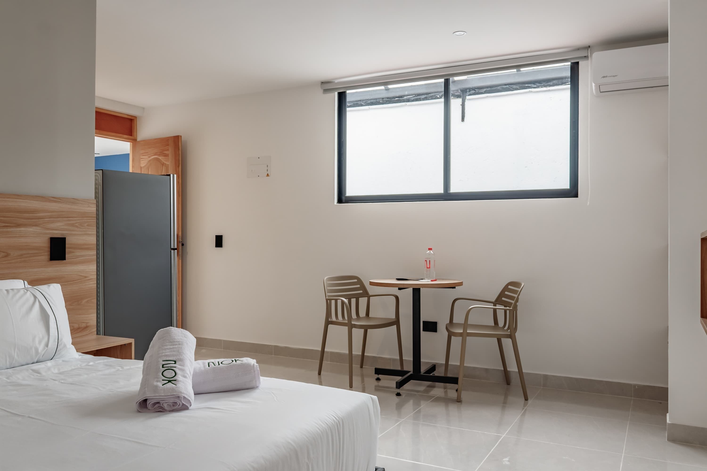 A hotel room with a bed, a small table with chairs, a window, and a door.