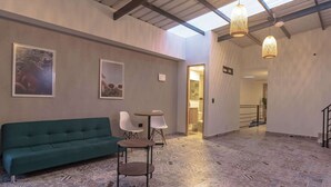 Ein geräumiger Raum mit einem grünen Sofa, zwei kleinen Tischen, Stühlen, einem gemusterten Boden und einem Oberlicht.