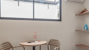 Ein Zimmer mit einem runden Tisch, zwei Stühlen, einer Wasserflasche und einem Fenster mit Blick auf ein Gebäude.