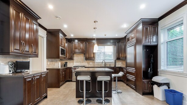 A modern kitchen with dark wood cabinets, a central island with stools, a built-in oven, and a window providing natural light.