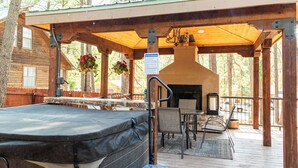 A covered outdoor deck with a hot tub, seating area, and a stone fireplace. - Royal Heaven (Ruidoso)