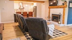 A living room with a fireplace, a dining area, and a kitchen in the background. - Royal Heaven (Ruidoso)