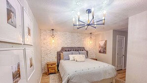 A bedroom with a large bed, a stone wall, a chandelier, and framed pictures on the wall. - Royal Heaven (Ruidoso)