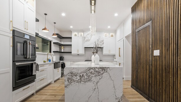Una cocina moderna con armarios blancos, una isla de mármol y una pared de acento de madera.