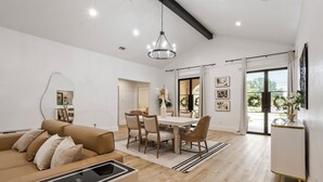 Una sala de estar moderna con sofá, mesa de comedor y sillas. Se aprecia un ventanal con vista a zonas verdes.