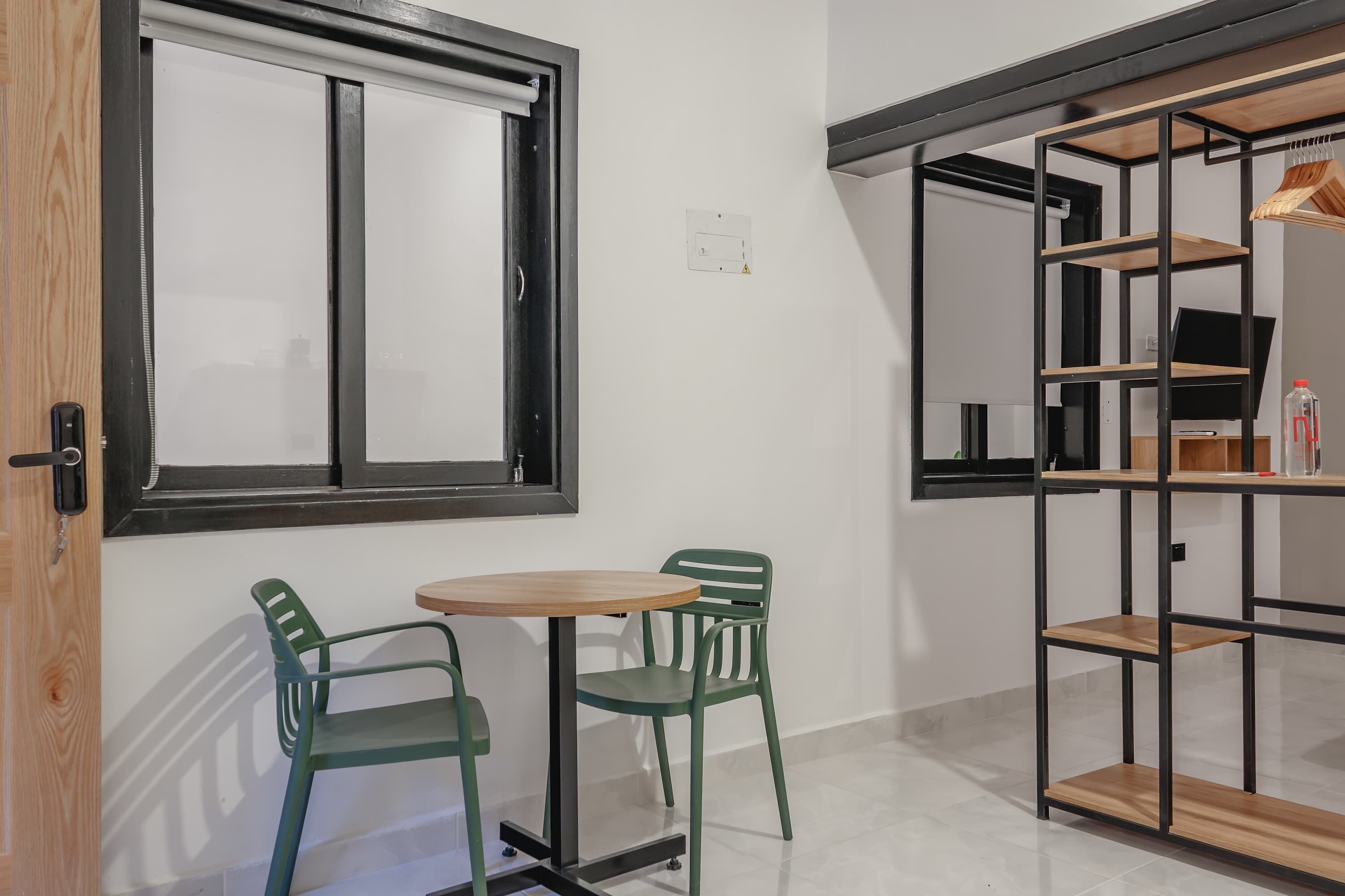 Una habitación pequeña con ventana, una mesa con dos sillas y un estante con un televisor y algunos objetos encima.