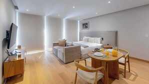 Ein modernes Hotelzimmer mit Bett, einer Couch, einem Esstisch mit Stühlen, einem Fernseher und einem kleinen Beistelltisch.