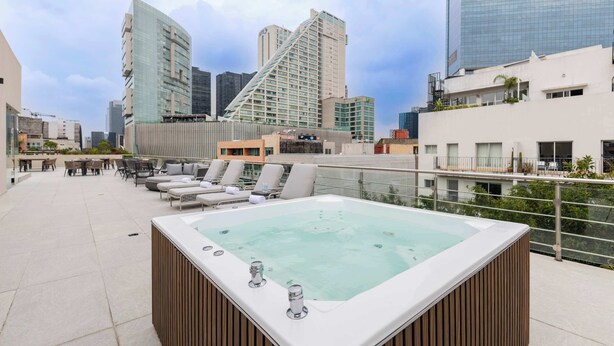 Eine Dachterrasse mit Whirlpool, Liegestühlen und Blick auf die Stadt.