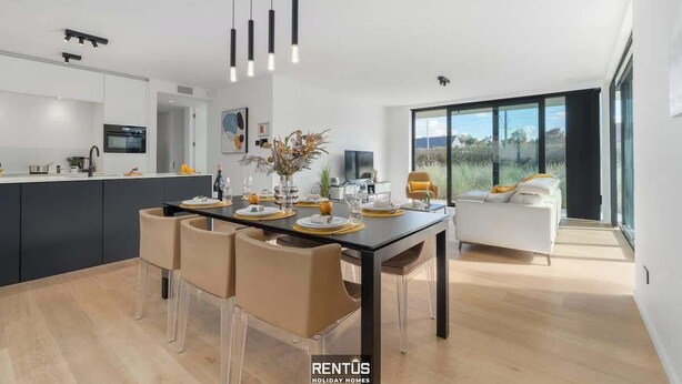 A modern kitchen with a dining area, large windows, and a view of the outdoors.