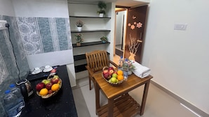 Un comedor con una mesa de madera, sillas y una cesta de frutas. Hay una botella de agua y un ordenador portátil sobre la mesa.