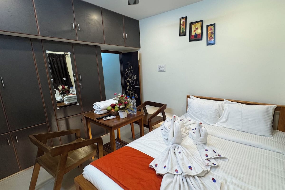 A hotel room with a bed, a wooden desk, a chair, a wardrobe, and three framed pictures on the wall.
