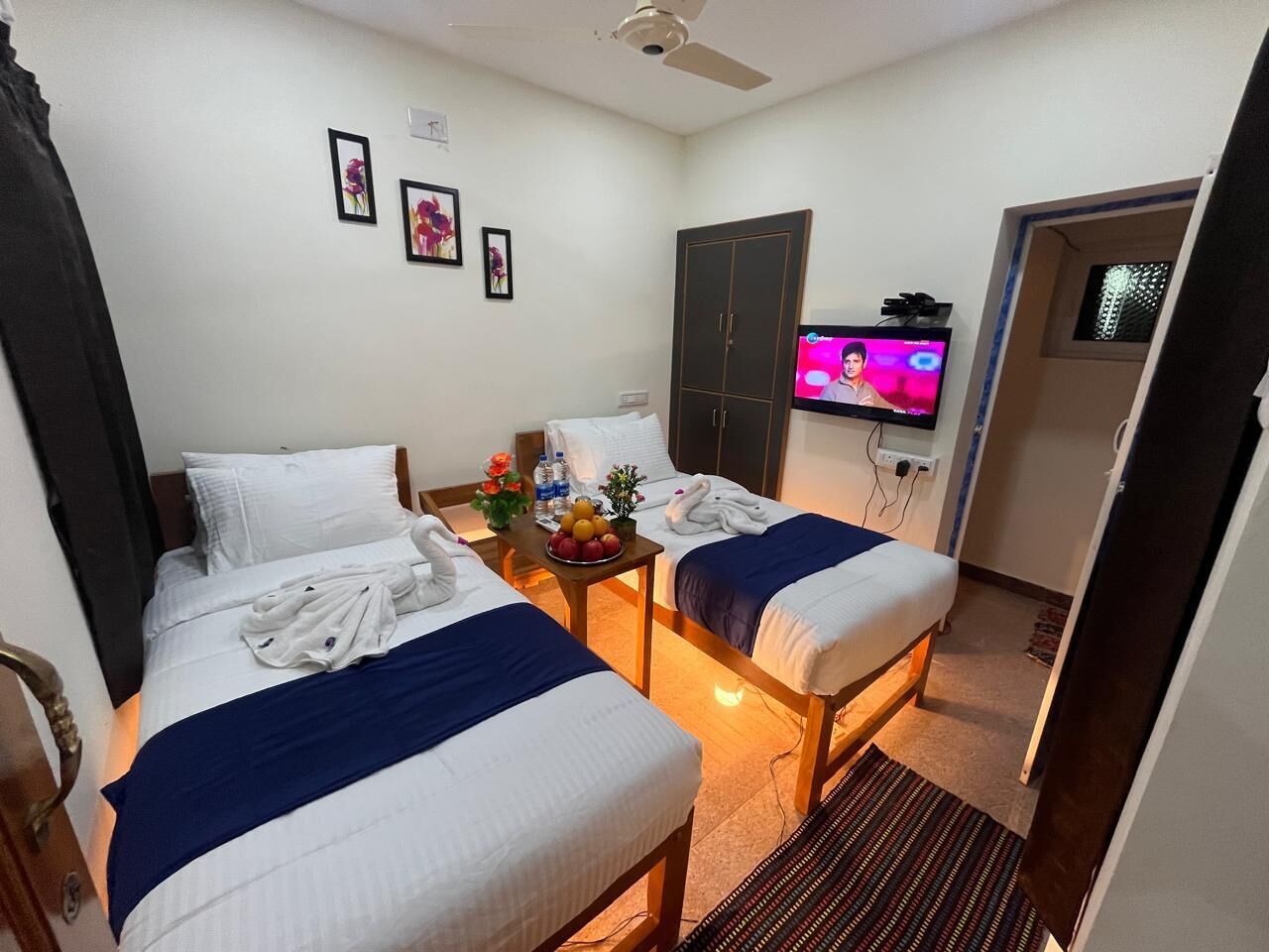 Une chambre d’hôtel avec deux lits, une télévision, une petite table avec des fruits et une porte donnant sur une autre chambre.
